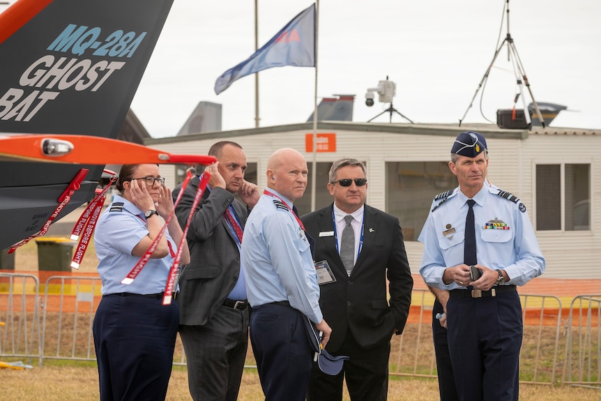 A group of five people in airforce formal uniforms next to a drone.
