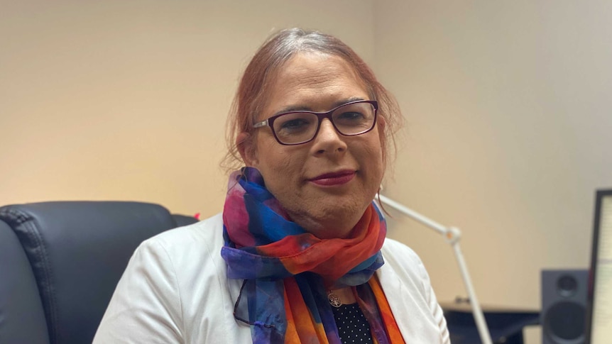 A peron with long hair wearing a scarf and a white shirt sitting at a computer