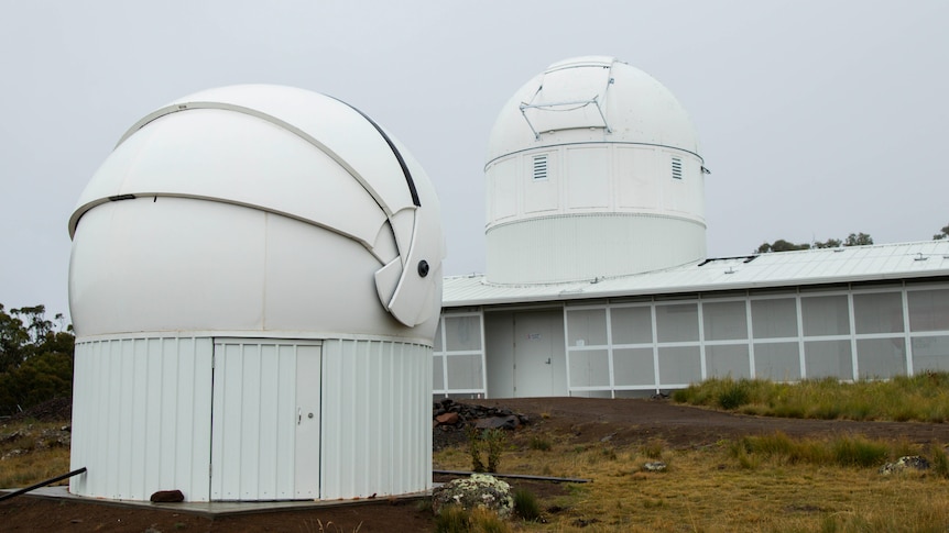 A white domed structure is seen in front of a larger building with a dome on the roof.