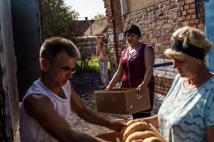 A woman holding a box while a man passes bread to another woman