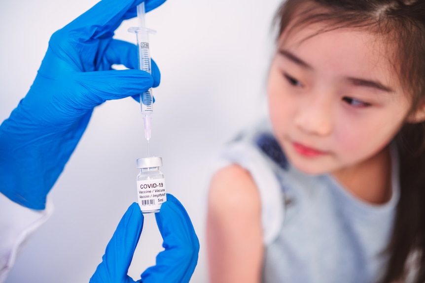 Hand with vial of COVID vaccine and young girl