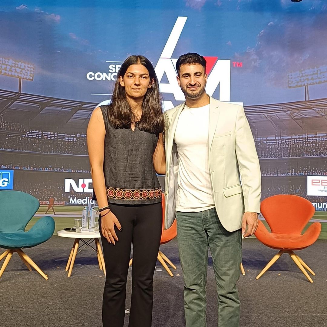 A woman and man pose for a photo in front of a photo of a grandstand.