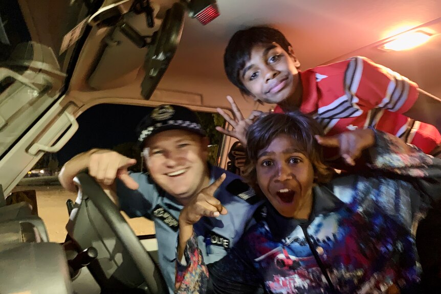 Two children and a police officer smiling and laughing in front seat of a police car