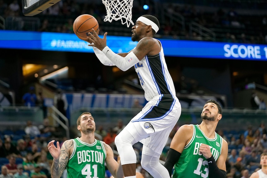 An NBA player goes up for a layup while two Boston Celtics players look on.