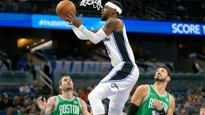 An NBA player goes up for a layup while two Boston Celtics players look on.