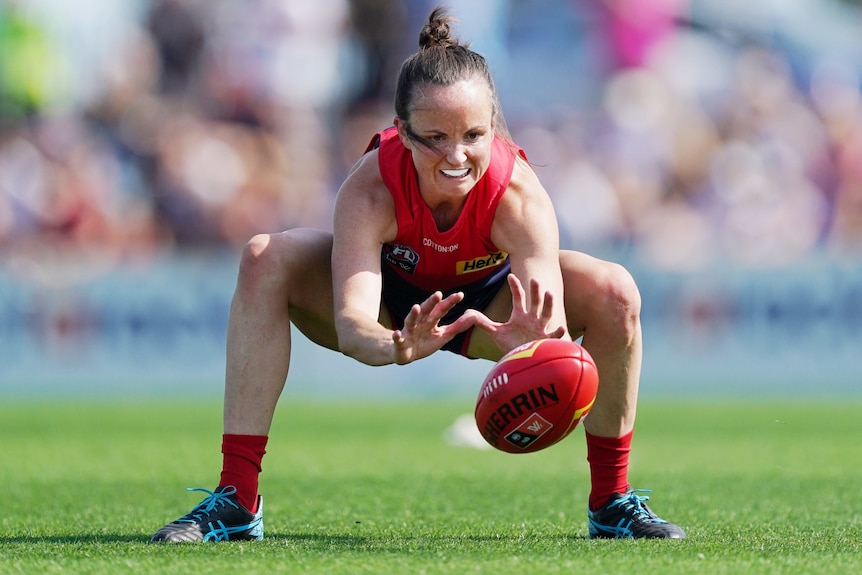 A Melbourne Demons AFLW player crouches as she attempts to retreive the ball.