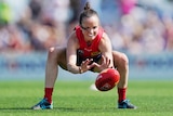 A Melbourne Demons AFLW player crouches as she attempts to retreive the ball.