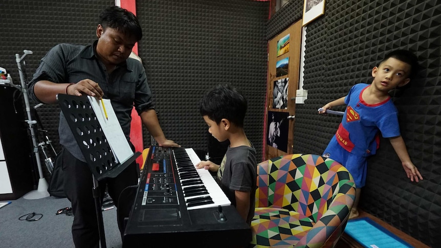 A man teaches two young boys how to play the keyboard.