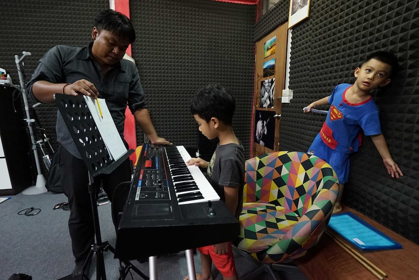 A man teaches two young boys how to play the keyboard.