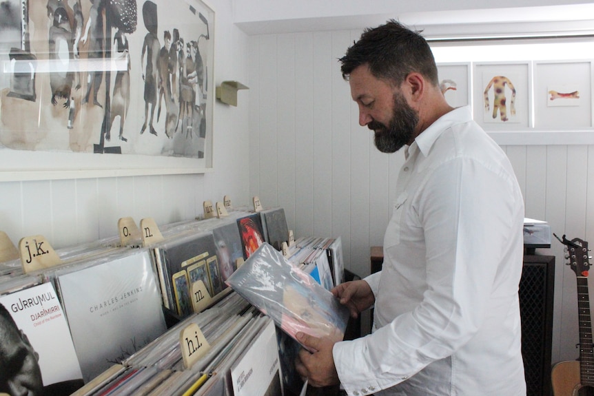 A man standing looking at a shelf full of vinyl records.