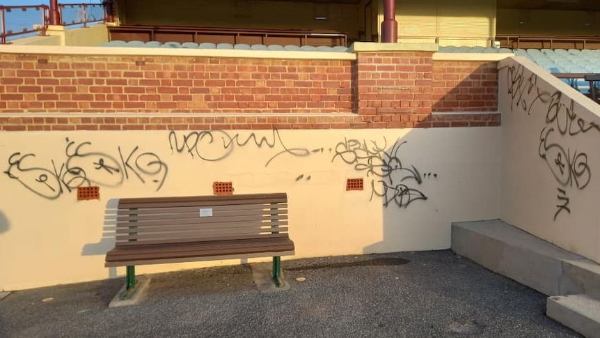 bench in front of grandstand with graffiti in black paint on cream walls