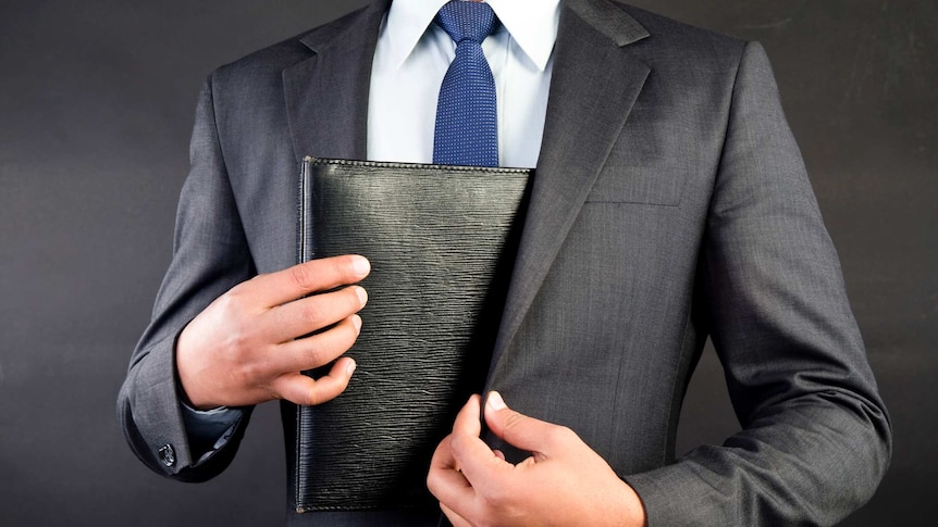 A suited man in a blue tie hides a business folder
