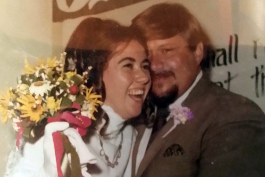 A woman, holding a bouquet stands cheek to cheek with a man, smiling.