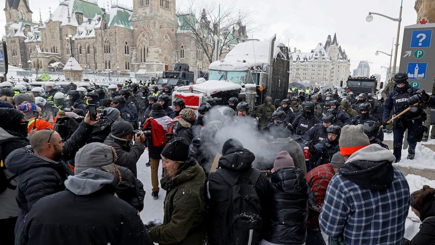 A crowd of people in the snow in front of a Parliament building. Some wear plain clothes, others are police.