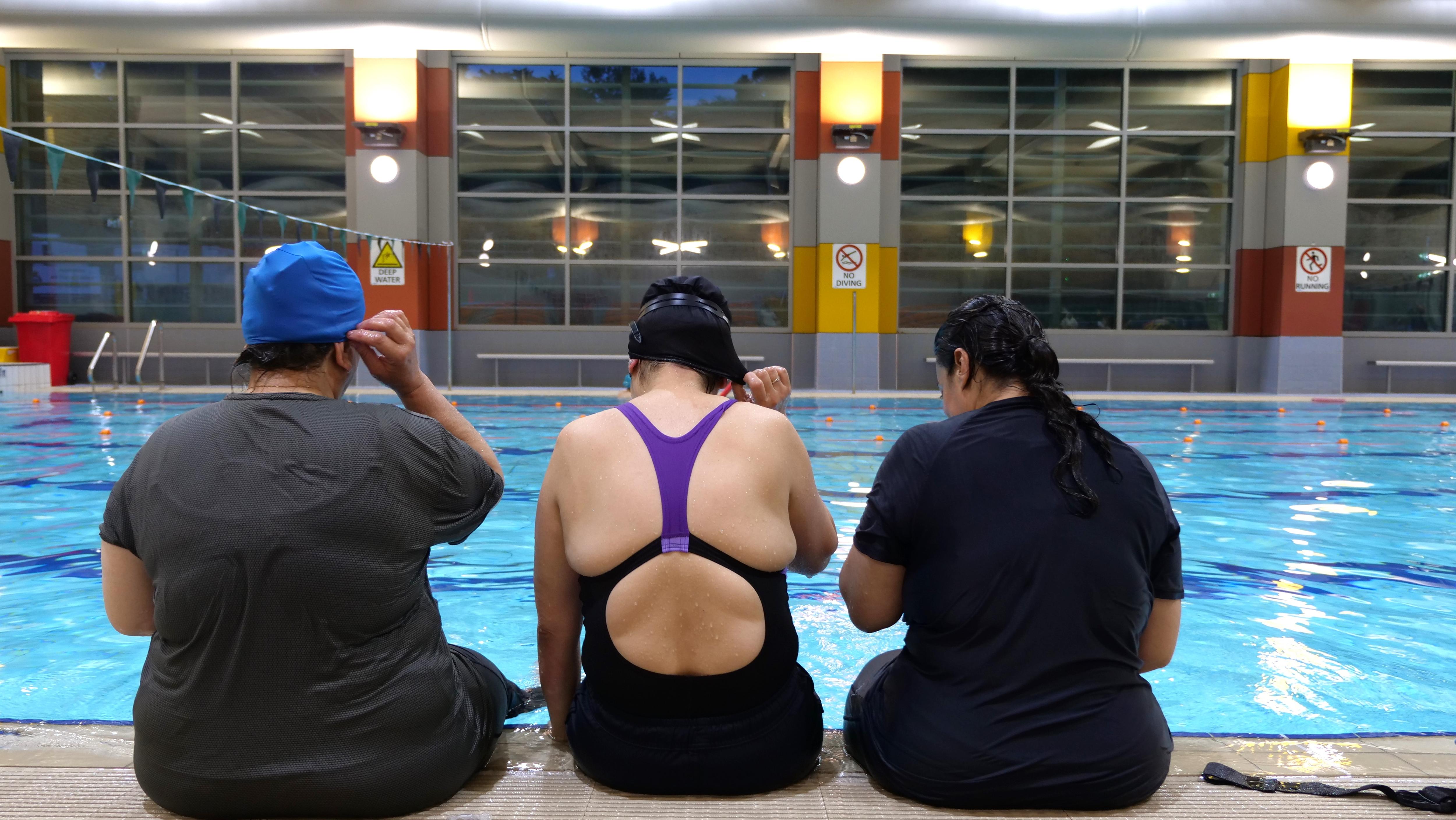 Three women sit at a pool edge
