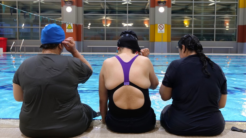 Three women sit at a pool edge