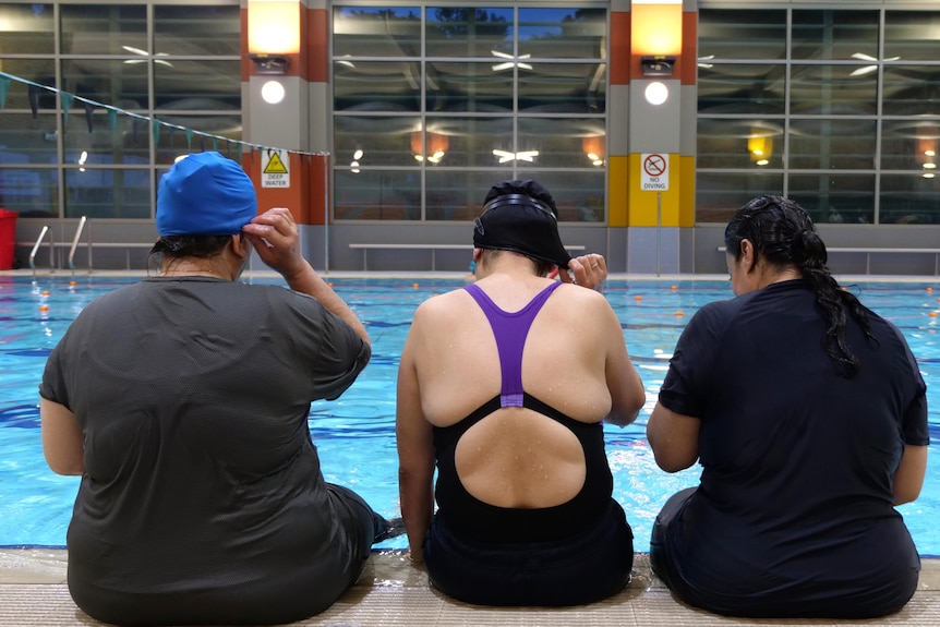 Three women sit at a pool edge
