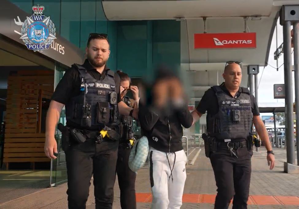A man whose face is blurred is escorted by police at Perth Airport.