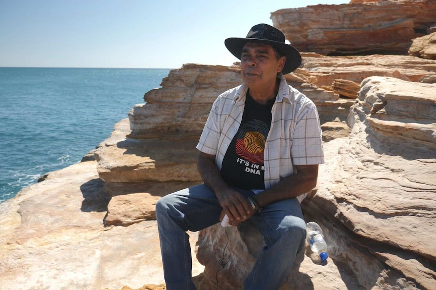 A man sitting on rocks by the sea.