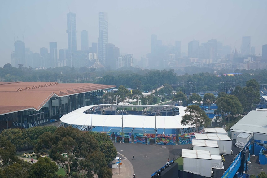 The Melbourne skyline is seen through a smoke haze with the Australian Open tennis courts in the foreground.