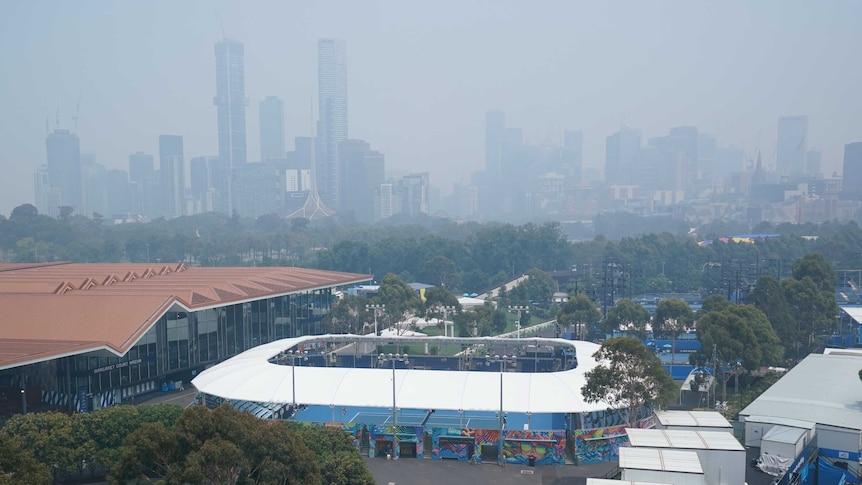 The Melbourne skyline is seen through a smoke haze with the Australian Open tennis courts in the foreground.