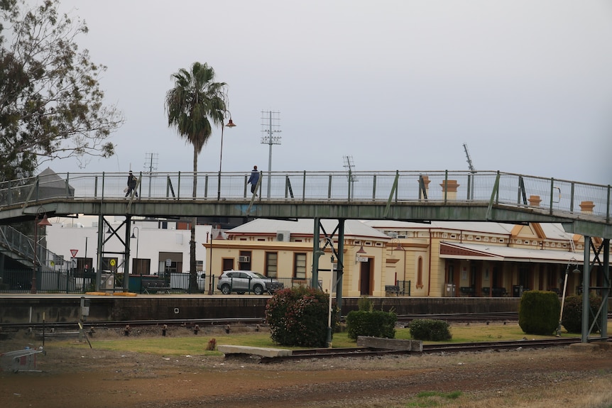 Un pont piétonnier ferroviaire avec une gare en arrière-plan