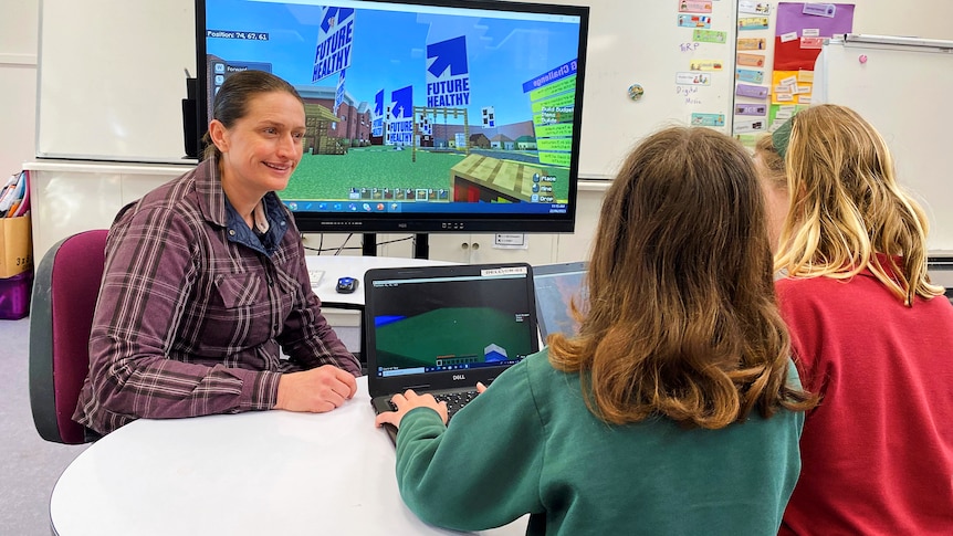 two students with back to camera face a smiling teacher and bigger screen with minecraft future healthy 