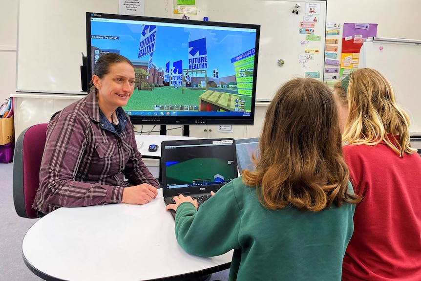two students with back to camera face a smiling teacher and bigger screen with minecraft future healthy 