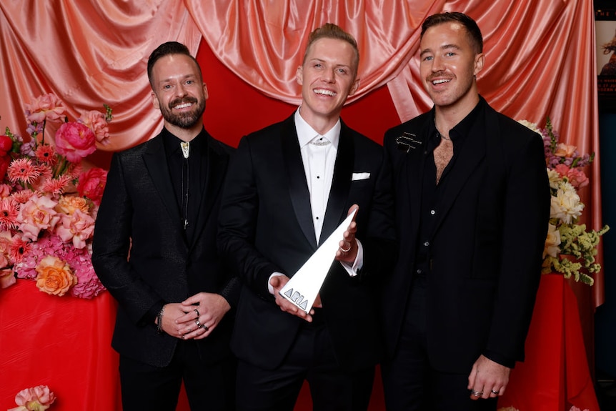 three members of rufus du sol pose with aria trophy in front of red coloured wall
