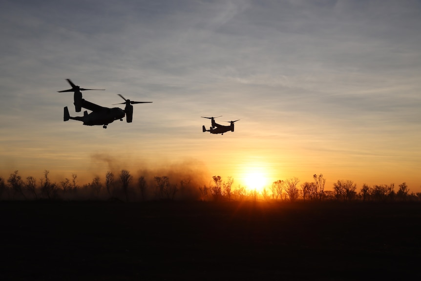 Two half-plane half-helicopter aircraft flies about bush and smoke with a sunset back drop