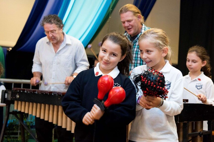 Children pose with maracas in front of marimbas.