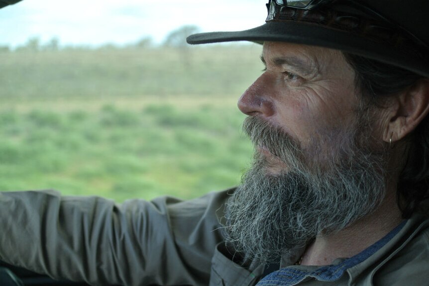 Profile shot of Tony Hill driving a car with green grass in background.