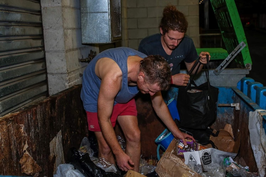 Two men rifle through a dumpster in Brisbane to fill up bags with food