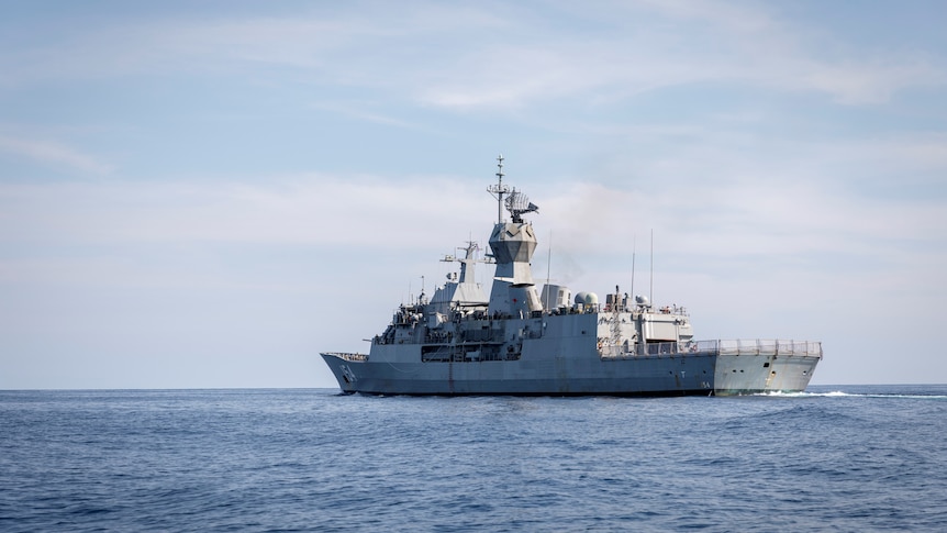 A large grey navy ship sails across the ocean