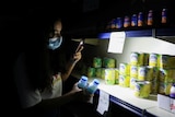 A customer uses her phone's torch light in a grocery store during a power cut