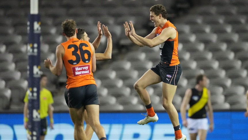 An AFL goalscorer leaps in the air in delight to high-five a teammate.