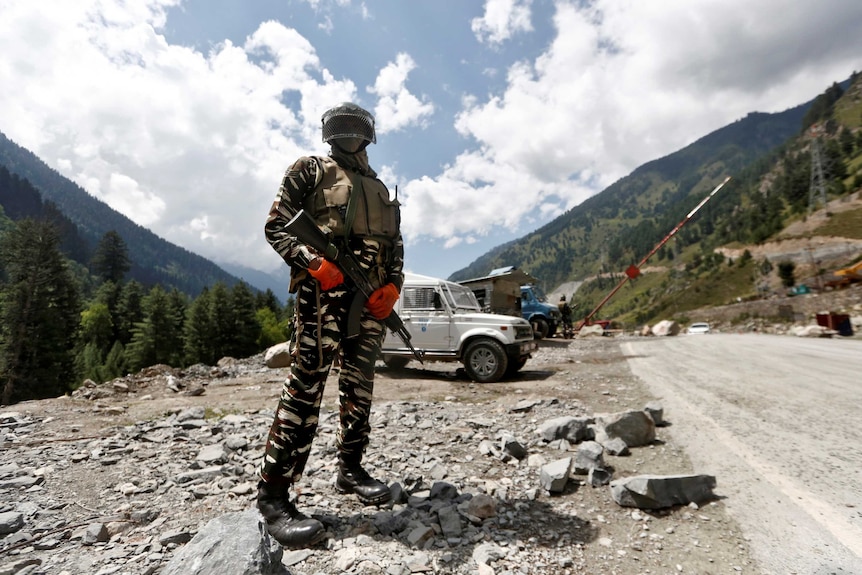 Мужчина в армейской форме стоит перед джипом и горами.