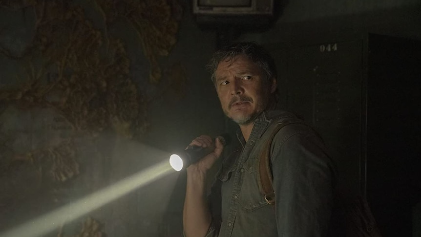 Pedro Pascal as Joel in HBO's The Last of Us holds a flashlight and looks over his shoulder.
