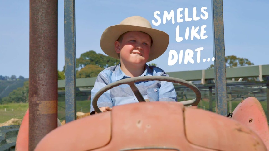 Boy sits on tractor, text overlay reads "Smells like dirt"