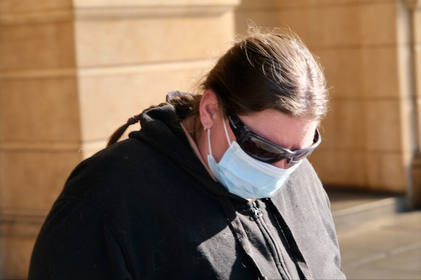A woman wearing a mask and sunglasses walks.