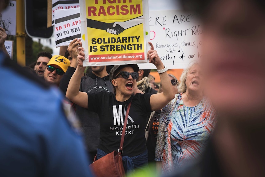 A group of left wing protesters stand shouting and holding placards opposite a rival group.