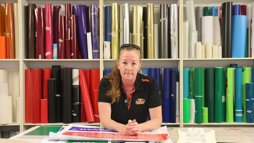 Deb Taipale leans on a table in front of shelves of brightly coloured folders