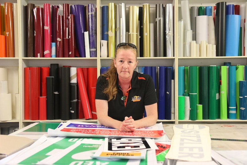 Deb Taipale leans on a table in front of shelves of brightly coloured folders