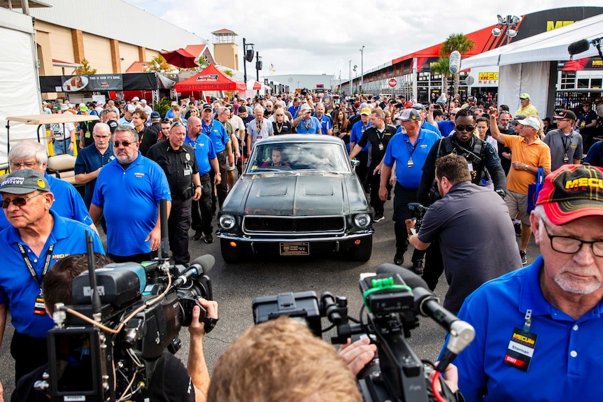 people walk past the green mustang as tv cameras film the car