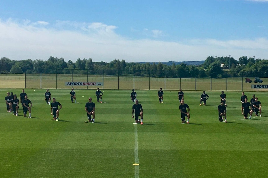 You few soccer players on a soccer field in a circle and all standing on one knee.