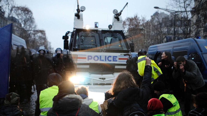 Demonstrators sit in front of a police water cannon on the Champs-Elysees avenue.