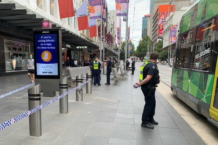 A blue and white strip of police tape is wrapped around steel bollards at a CBD open pedestrian mall.