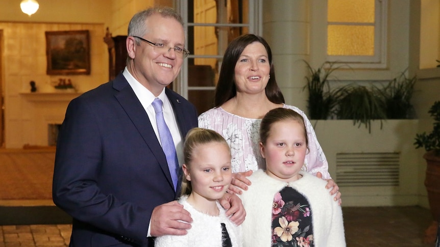 Scott Morrison stands next to his wife, and two young daughters, all smiling at the camera.