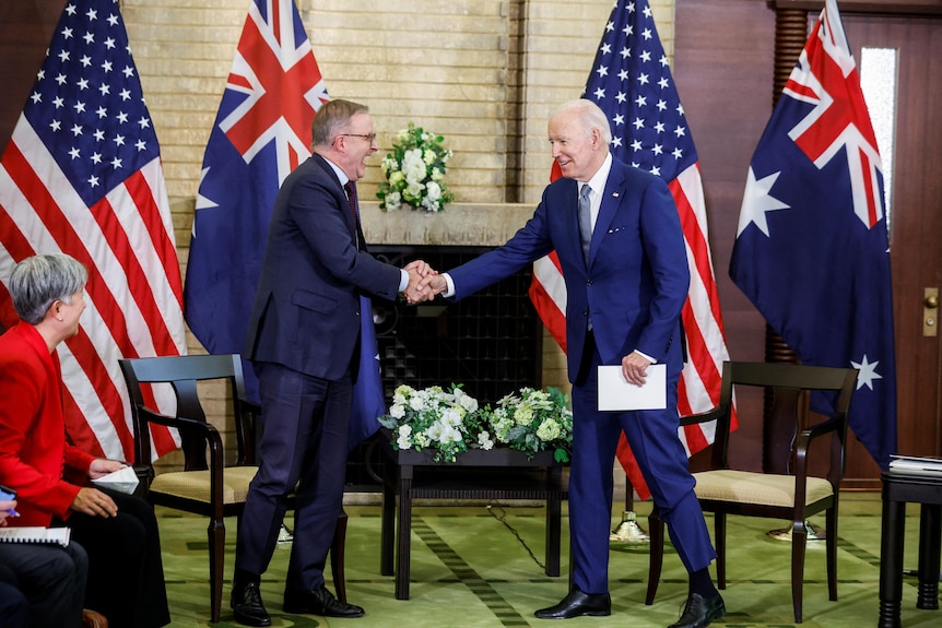 Two men standing in front of flags, shaking hands.