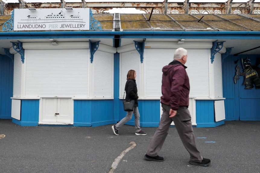 People walk past a jewellery shop with its shutters closed in Wales.